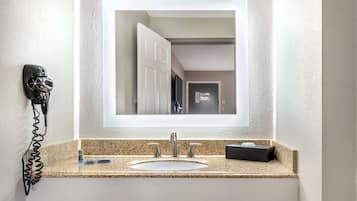 A bathroom with a granite countertop, a white sink, a mirror, a hairdryer, and a small box on the counter.