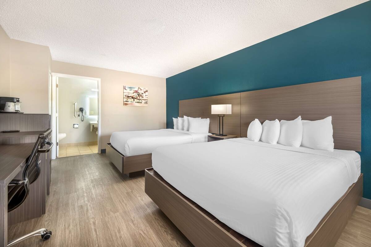 A hotel room with two beds, a desk, and a shower area.