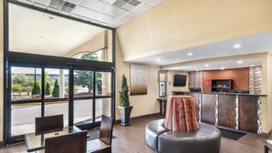 A hotel lobby with a seating area, a reception desk, and a large window offering a view of the street.