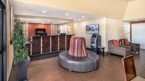 A reception area with a reception desk, a seating area with a round ottoman, a television mounted on the wall, and a potted plant.
