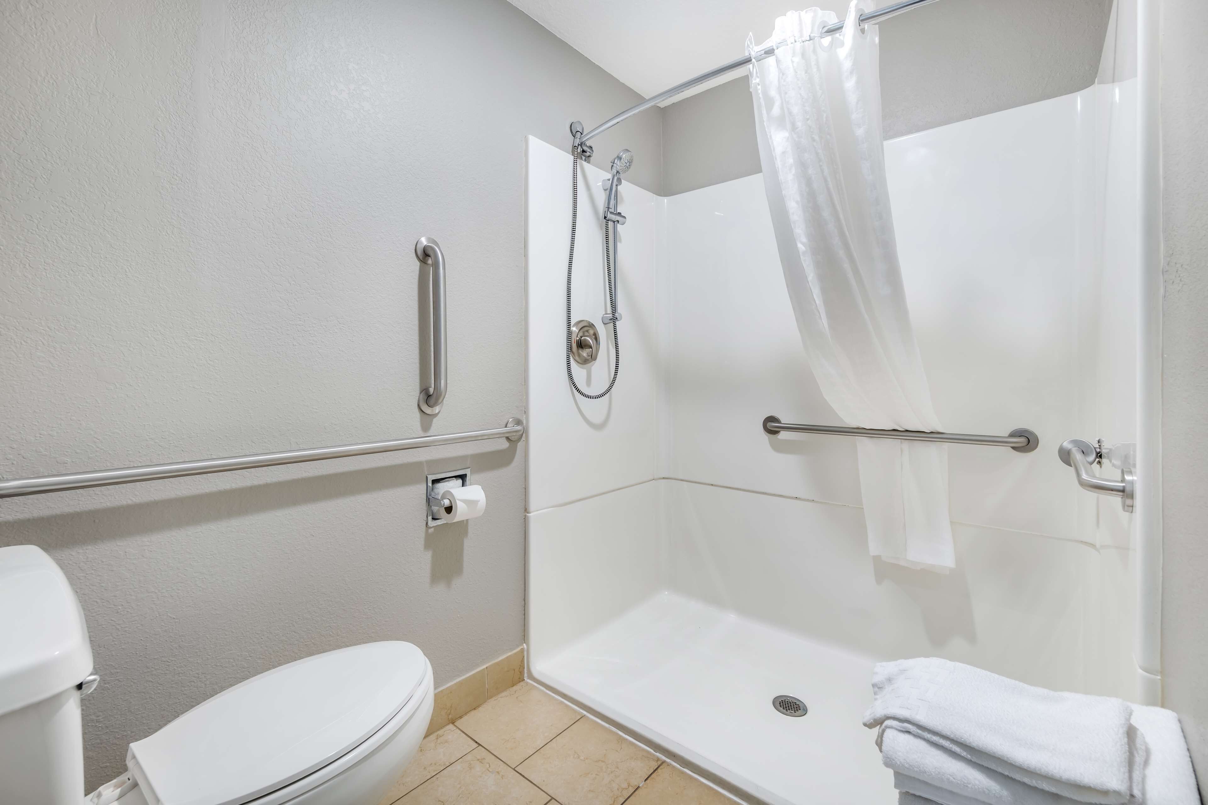 Un baño con inodoro blanco, ducha con puerta de cristal y barra de apoyo.