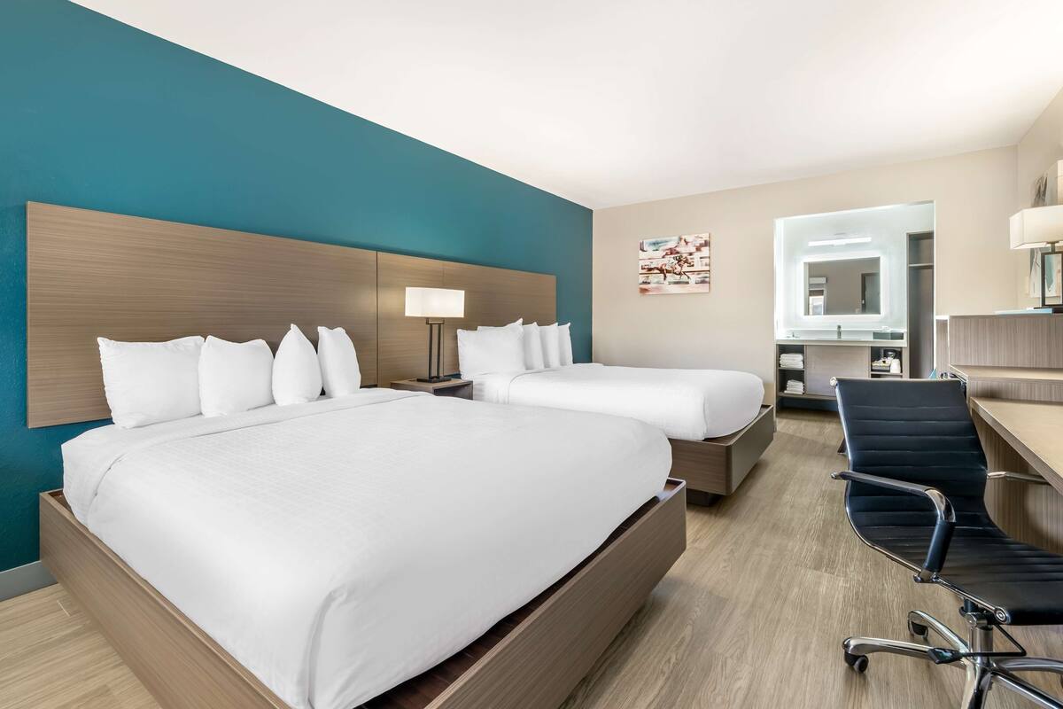 A hotel room with two beds, a desk, a chair, a lamp, and a mirror.