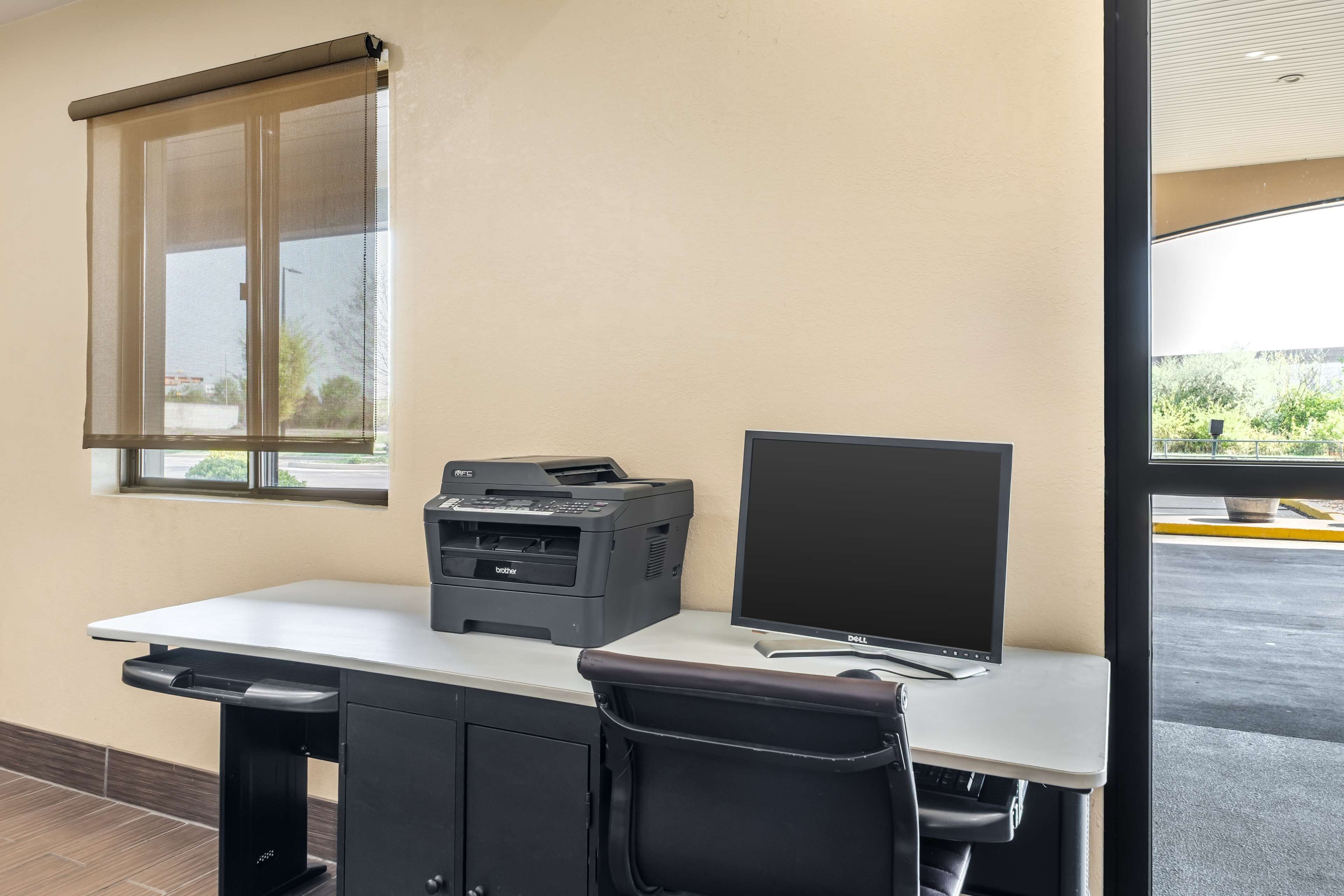 Uma mesa com impressora, monitor e cadeira em um quarto com janela e vista para o exterior.