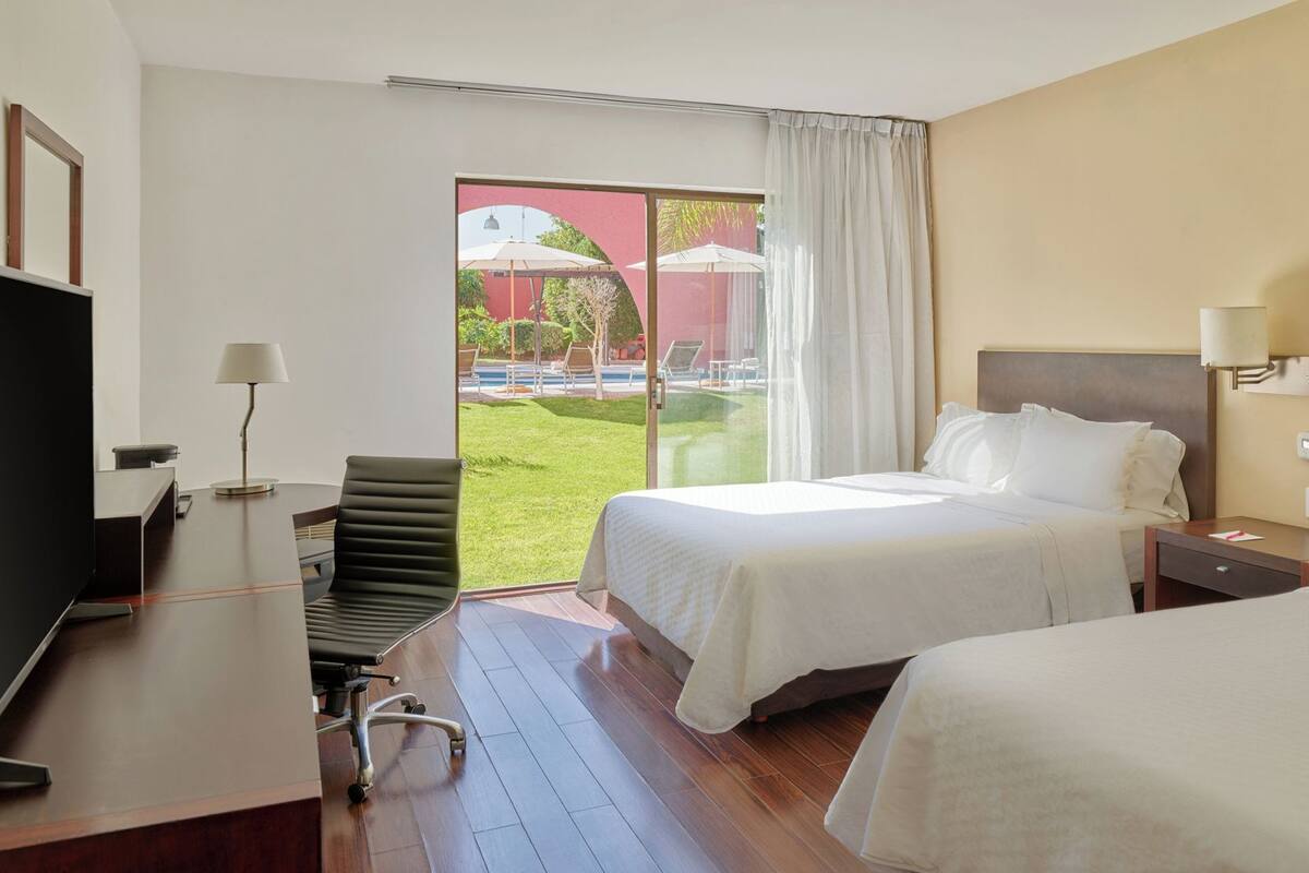 Quarto de hotel com cama, escrivaninha, cadeira e televisão.