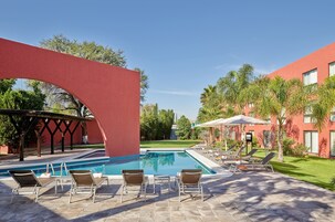 Una piscina con sillones de descanso y una pérgola.