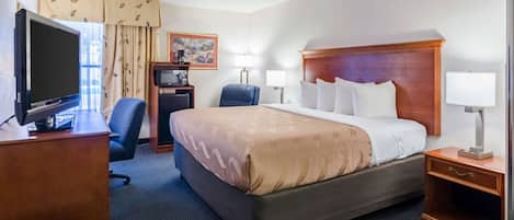 Habitación de hotel con una cama grande, un escritorio con televisor, una silla, una lámpara de escritorio y una mesita de noche.