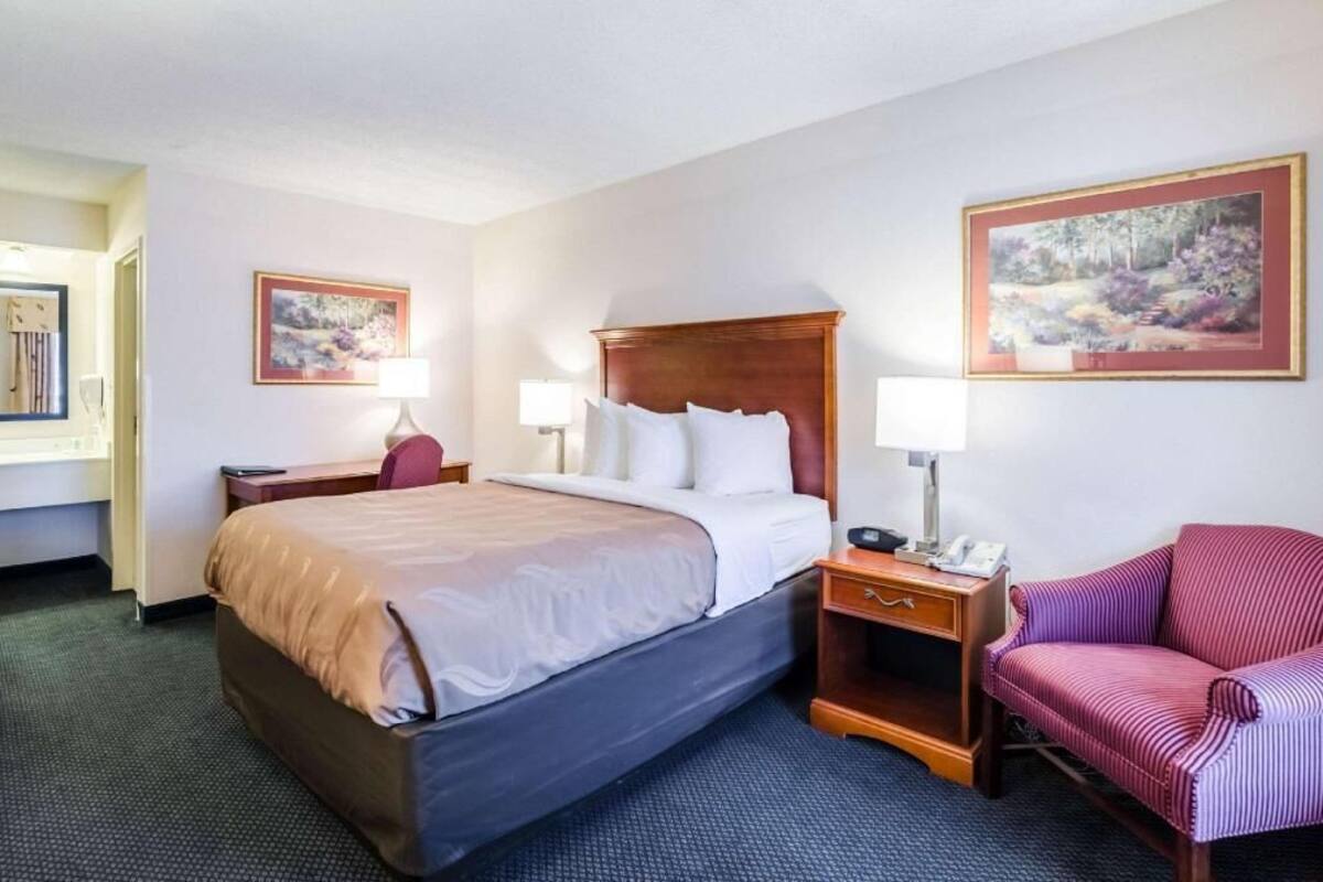 A hotel room with a large bed, bedside tables, a chair, and two paintings on the walls.