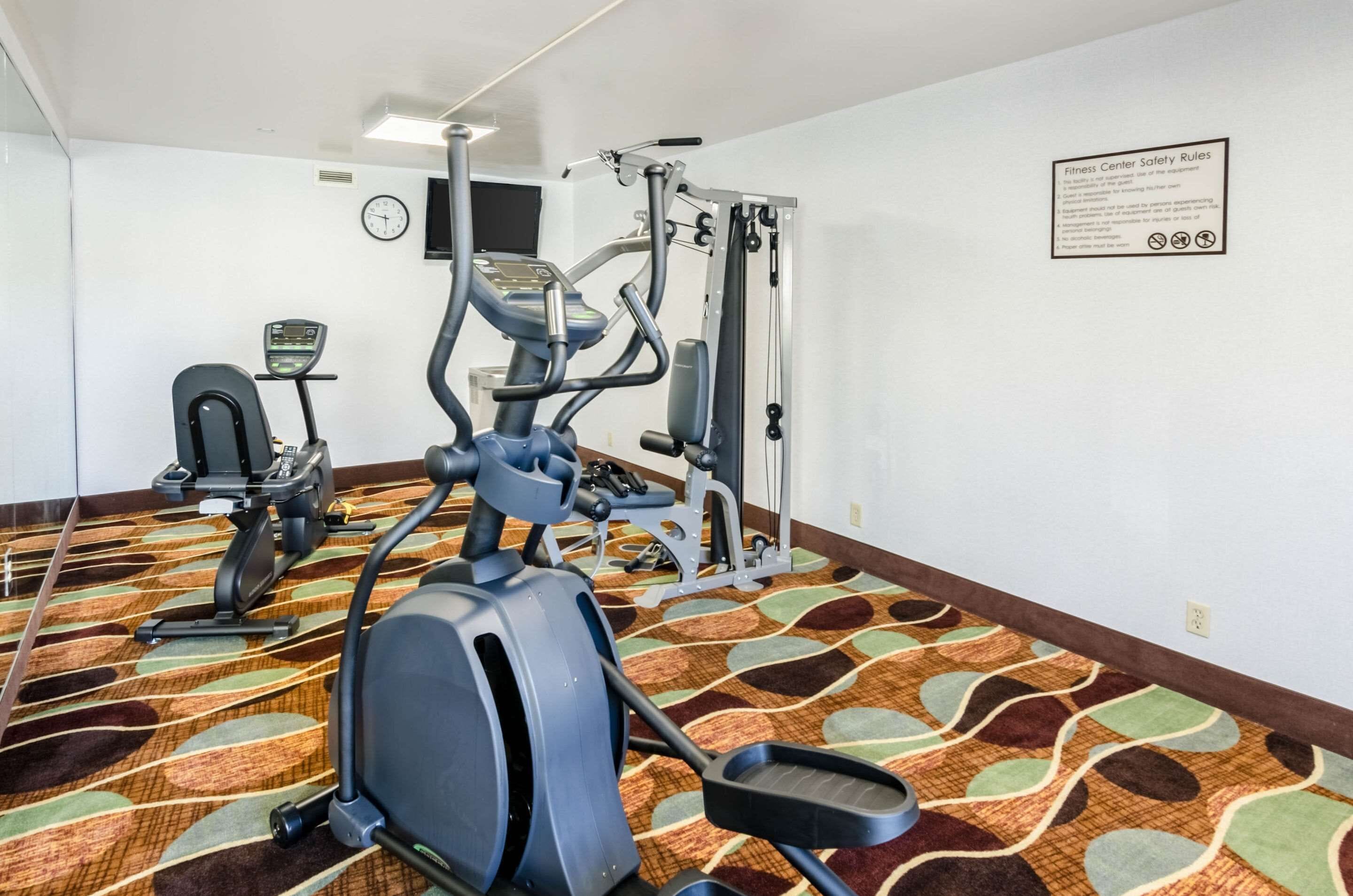 A fitness center with cardio machines, weight training equipment, and a wall-mounted clock.