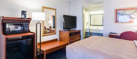 A hotel room with a bed, a TV, a microwave, a coffee maker, a desk, and a chair.