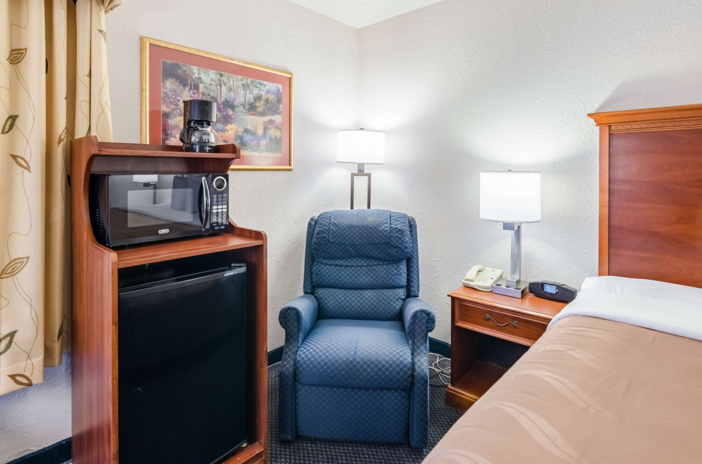 Une chambre d’hôtel équipée d’un lit, d’un bureau avec une lampe, d’une chaise, d’un four à micro-ondes et d’un réfrigérateur.