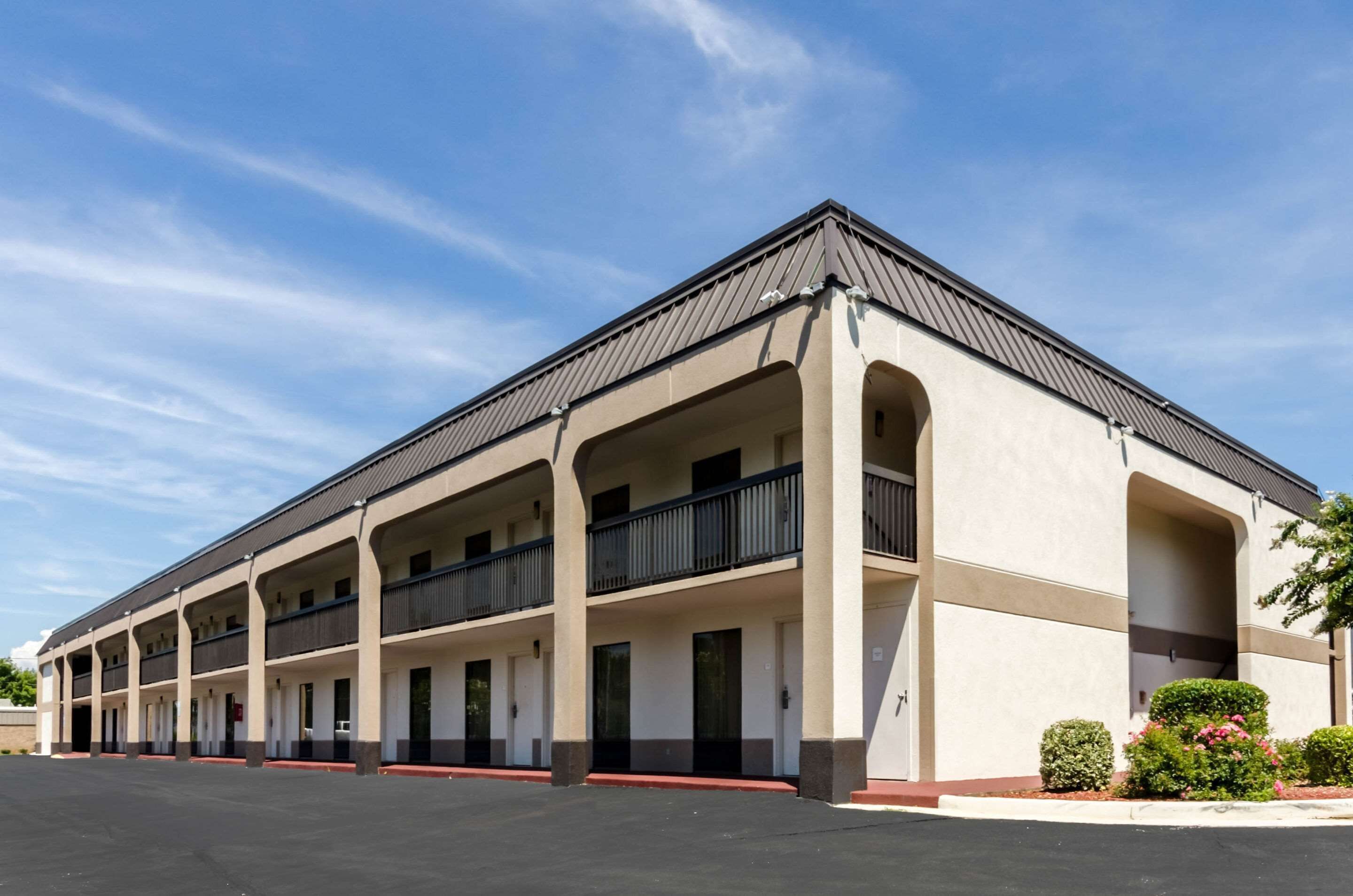 A multi-story motel with a flat roof, multiple balconies, and a parking lot in front.