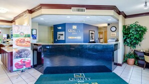 A hotel reception area with a blue counter, a clock, and a sign for Quality Inn by Choice Hotels in Lynchburg, VA.