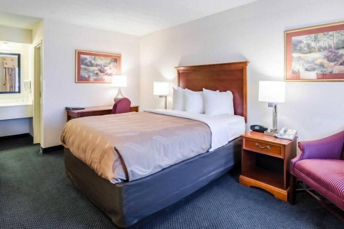 A hotel room with a large bed, bedside tables, a chair, and artwork on the walls.