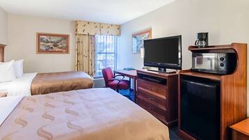 Een hotelkamer met twee bedden, een bureau met een computer, een televisie, een magnetron en een koffiezetapparaat.
