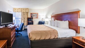 Une chambre d’hôtel avec un grand lit, un bureau équipé d’une télévision, d’un ordinateur et d’une chaise.