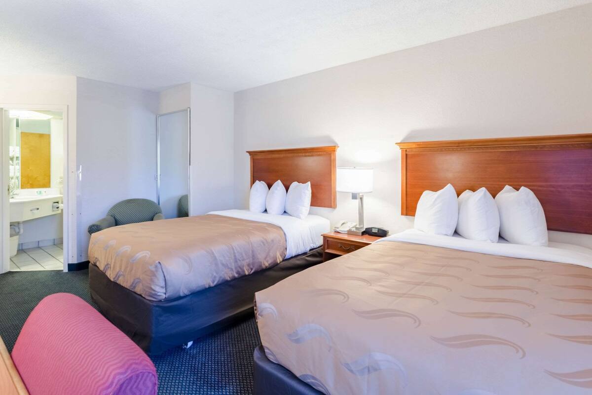 A hotel room with two beds, a desk, a chair, and a bathroom.