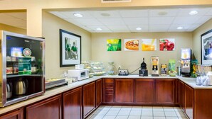 A self-service breakfast area with a coffee machine, juice dispenser, and various food items.