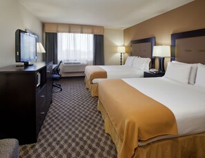 A hotel room with two beds, a desk with a television, and a window with curtains.