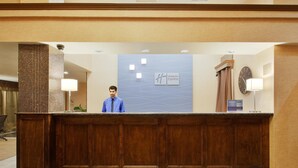 A hotel reception desk with a wooden panel design, a clock, and a sign for Holiday Inn Express.
