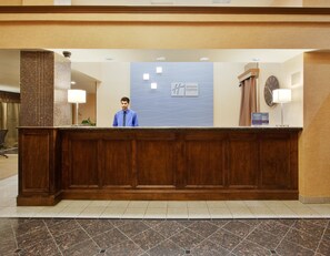 A hotel reception desk with a wooden panel design, a clock, and a sign for Holiday Inn Express.