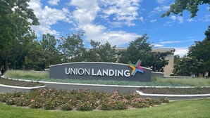 A sign for Union Landing with a colorful star logo, surrounded by well-maintained grass and flowering plants.