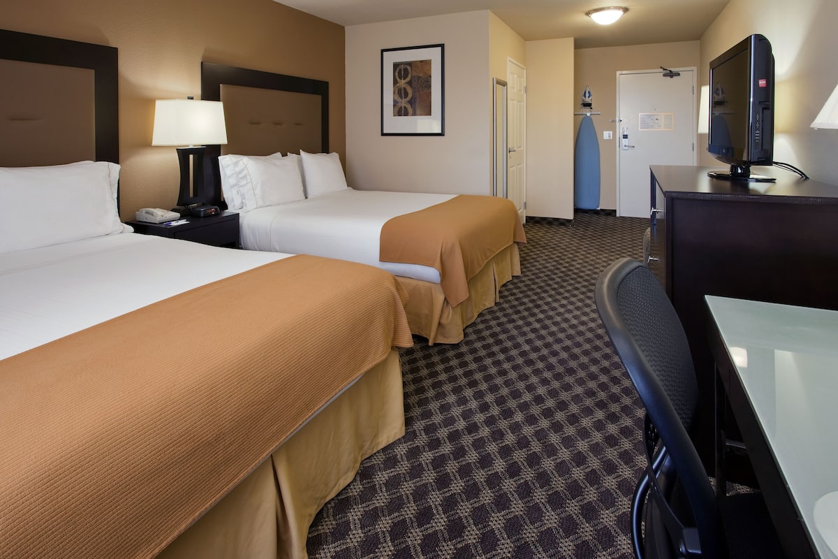 Quarto de hotel com duas camas, uma escrivaninha, televisão e porta do banheiro.