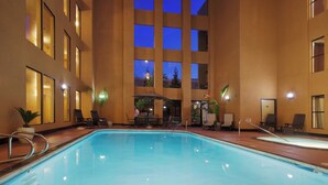 An indoor swimming pool with lounge chairs and tables, surrounded by a building with multiple windows and a night sky view. - Holiday Inn Express Union City (San Jose) by IHG (Union City)