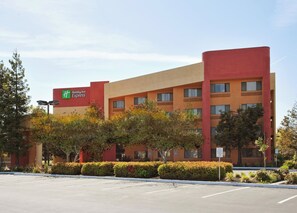 Een Holiday Inn Express hotel met een gevel in rood en beige, meerdere ramen en een parkeerplaats ervoor.