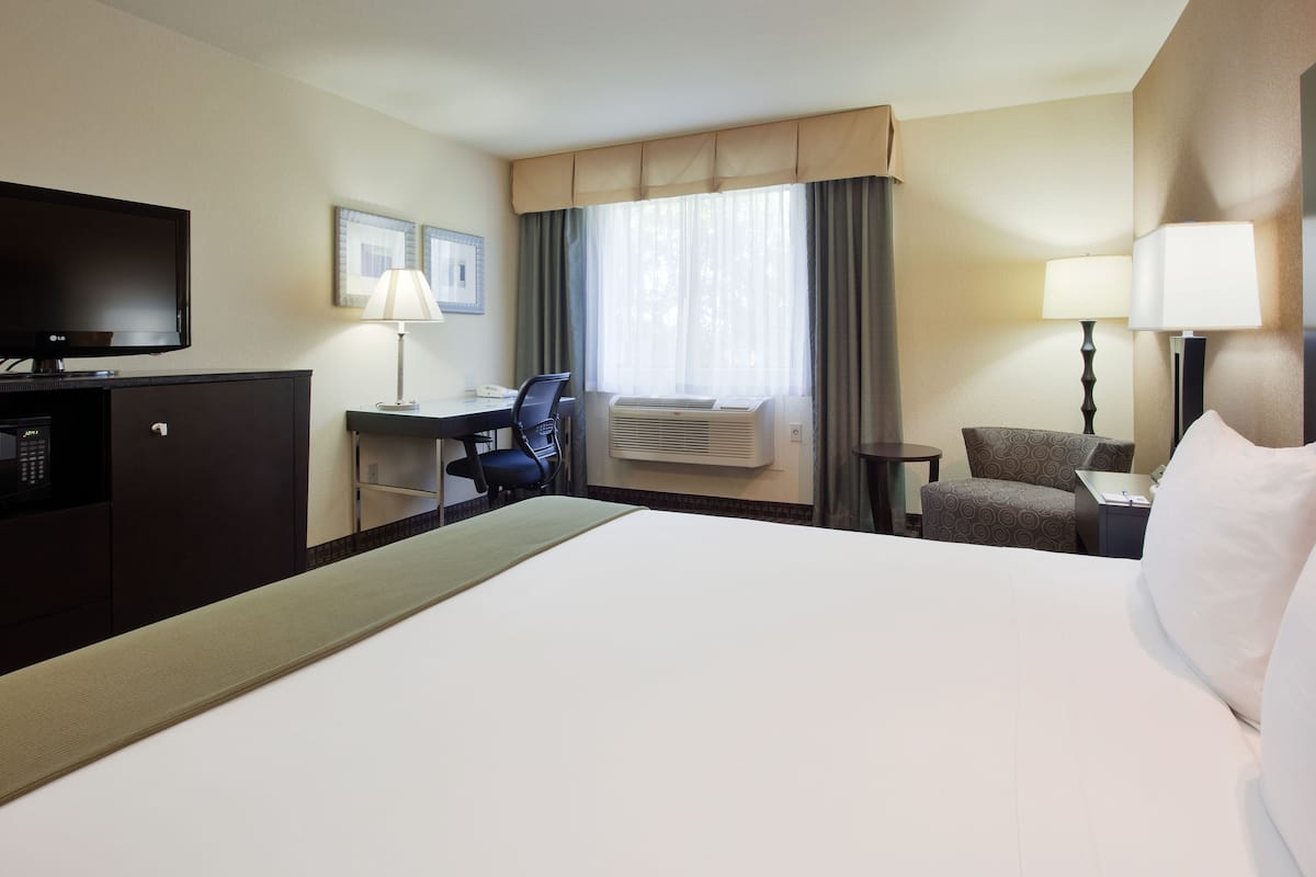 Quarto de hotel com cama, escrivaninha, cadeira, TV e ar condicionado.