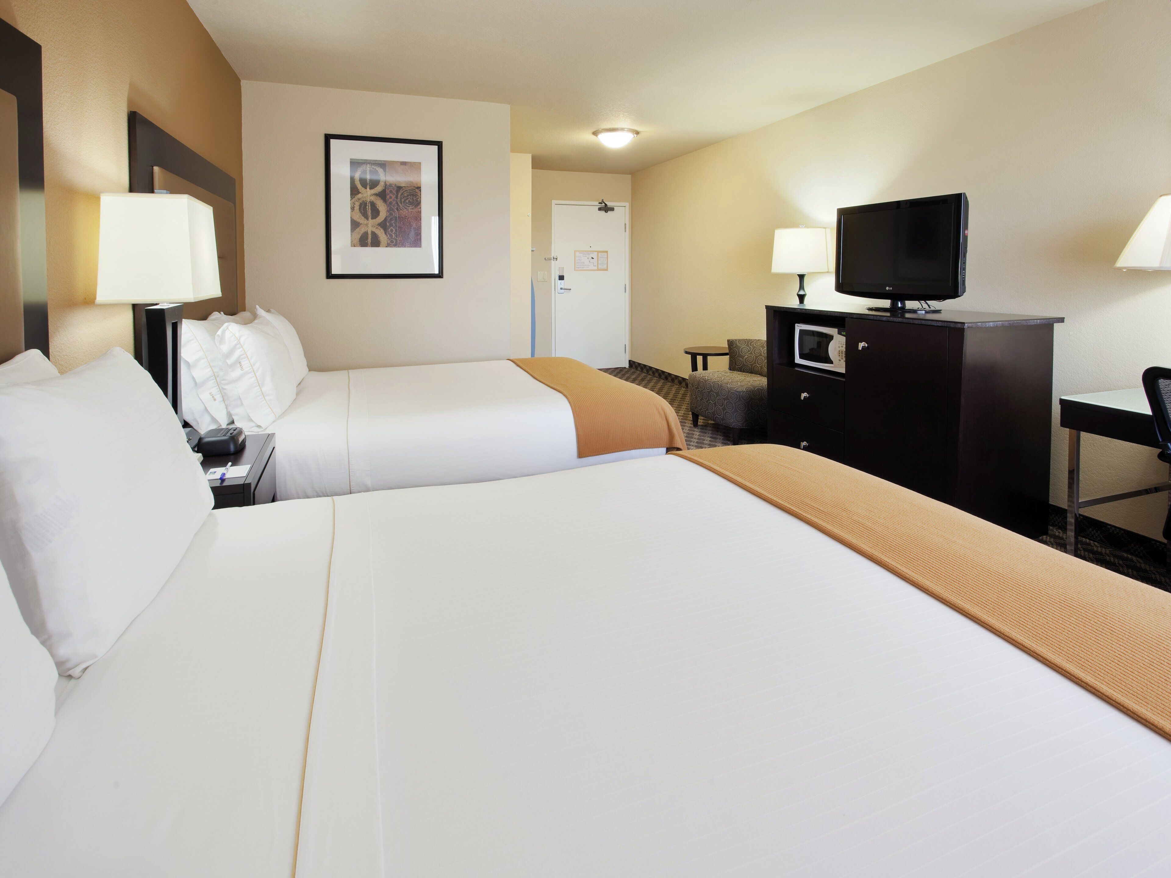 Habitación de hotel con dos camas, un escritorio, televisor, microondas y una silla.