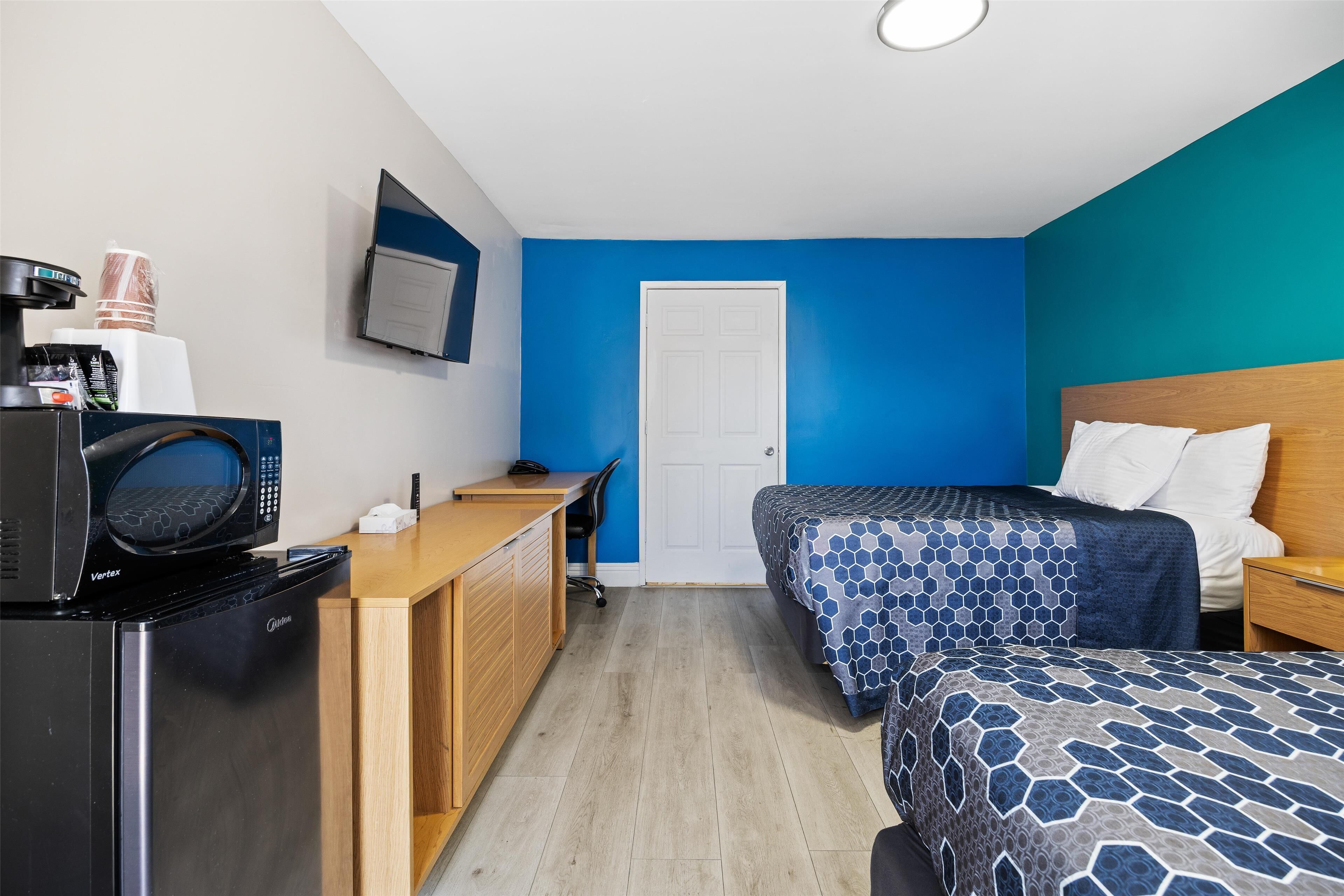 Habitación de hotel con kitchenette, cama con ropa de cama estampada, escritorio con silla y una puerta.