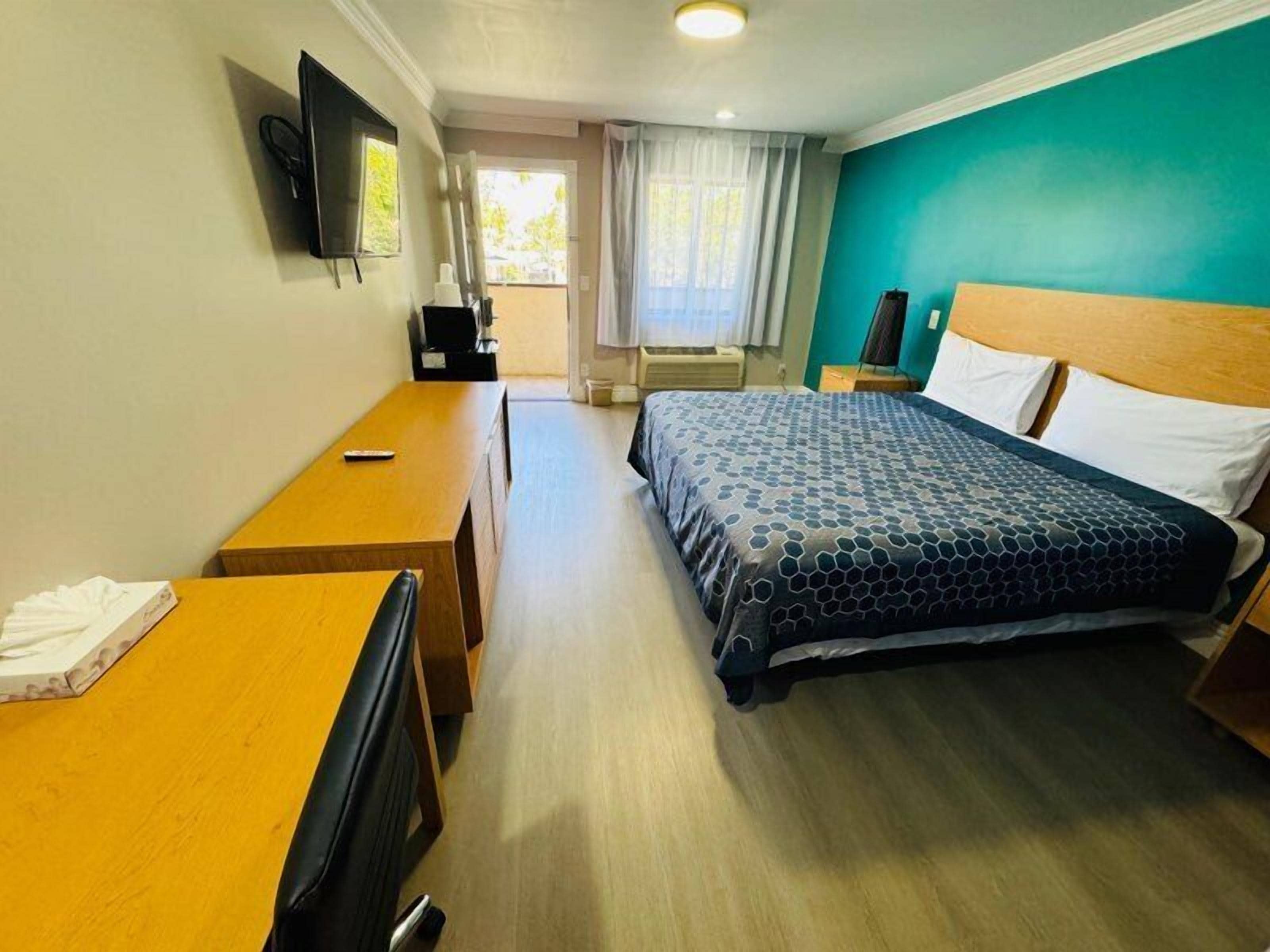 A hotel room with a bed, a desk, a chair, a television, and a window with curtains.