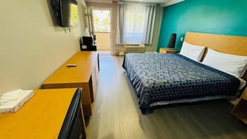 A hotel room with a bed, a desk, a chair, a television, and a window with curtains.