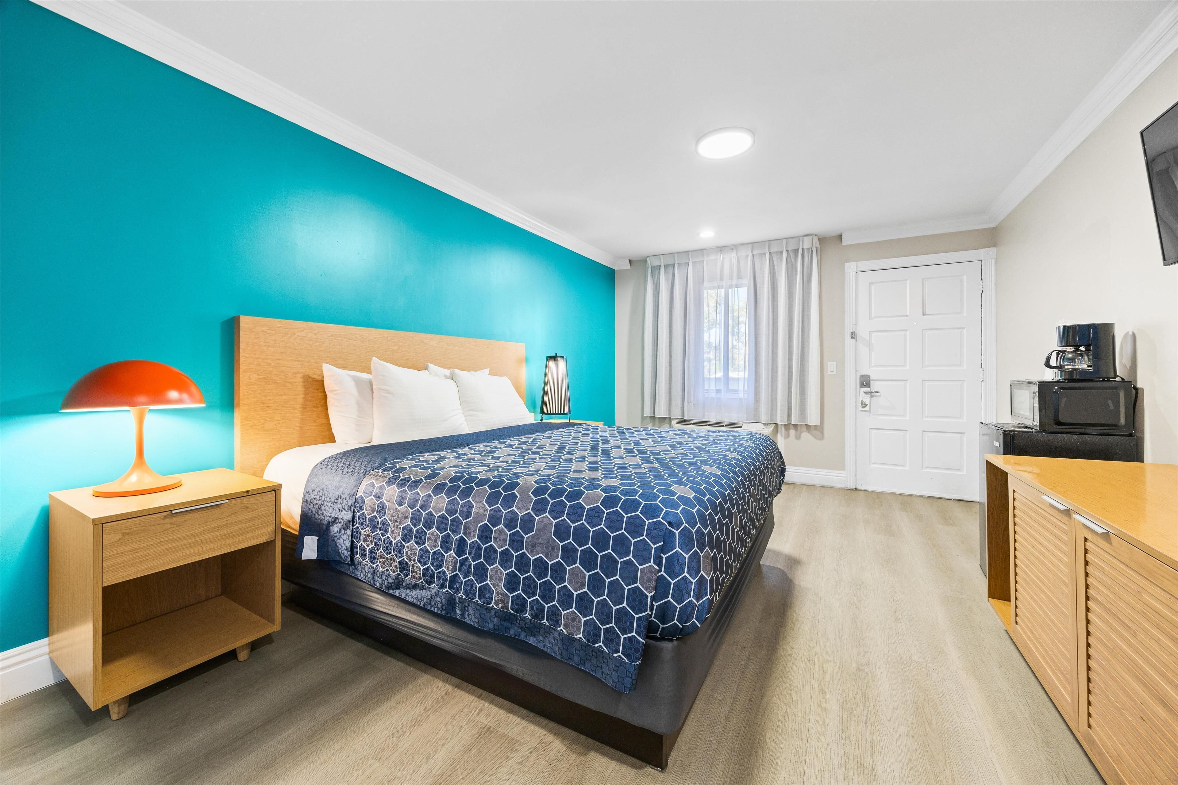 A modern hotel room with a bed, a nightstand, a desk, and a television.