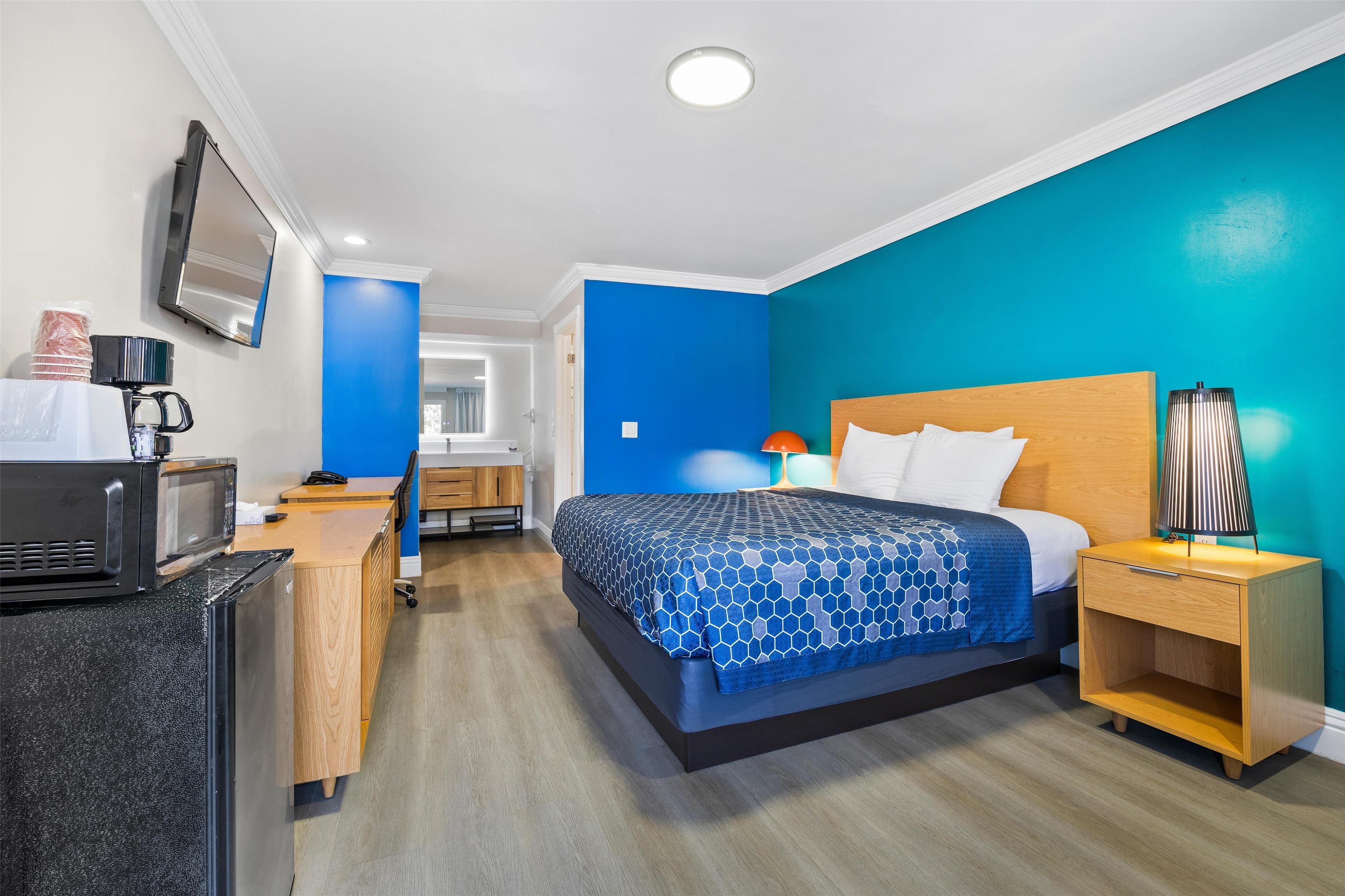 A hotel room with a bed, bedside table, and a desk with a microwave.
