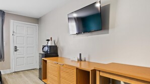 Huoneessa on puinen työpöytä, seinälle asennettu televisio, mikroaaltouuni ja ovi.