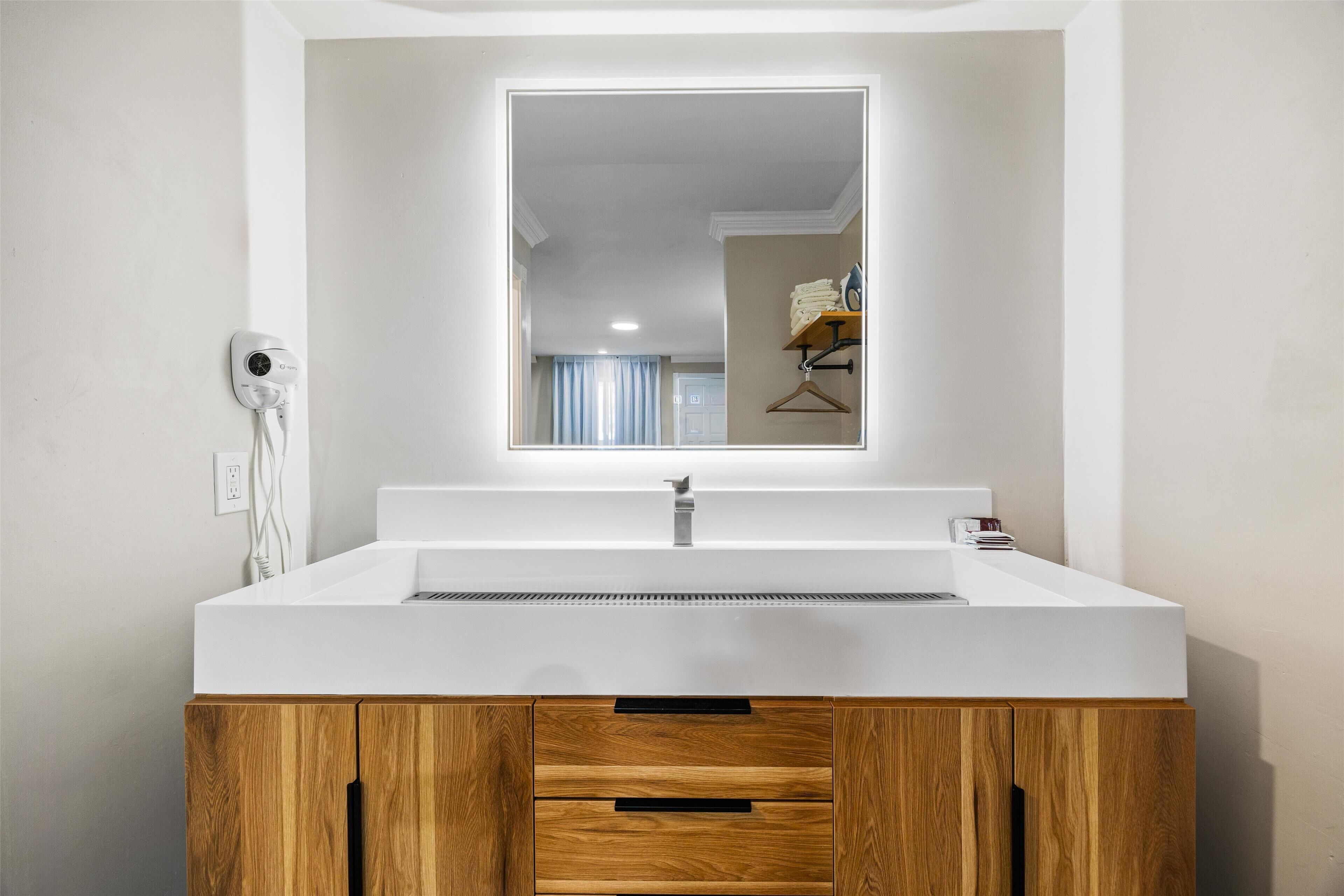 Un baño moderno con un lavabo blanco, un mueble de madera y un espejo sobre el lavabo.
