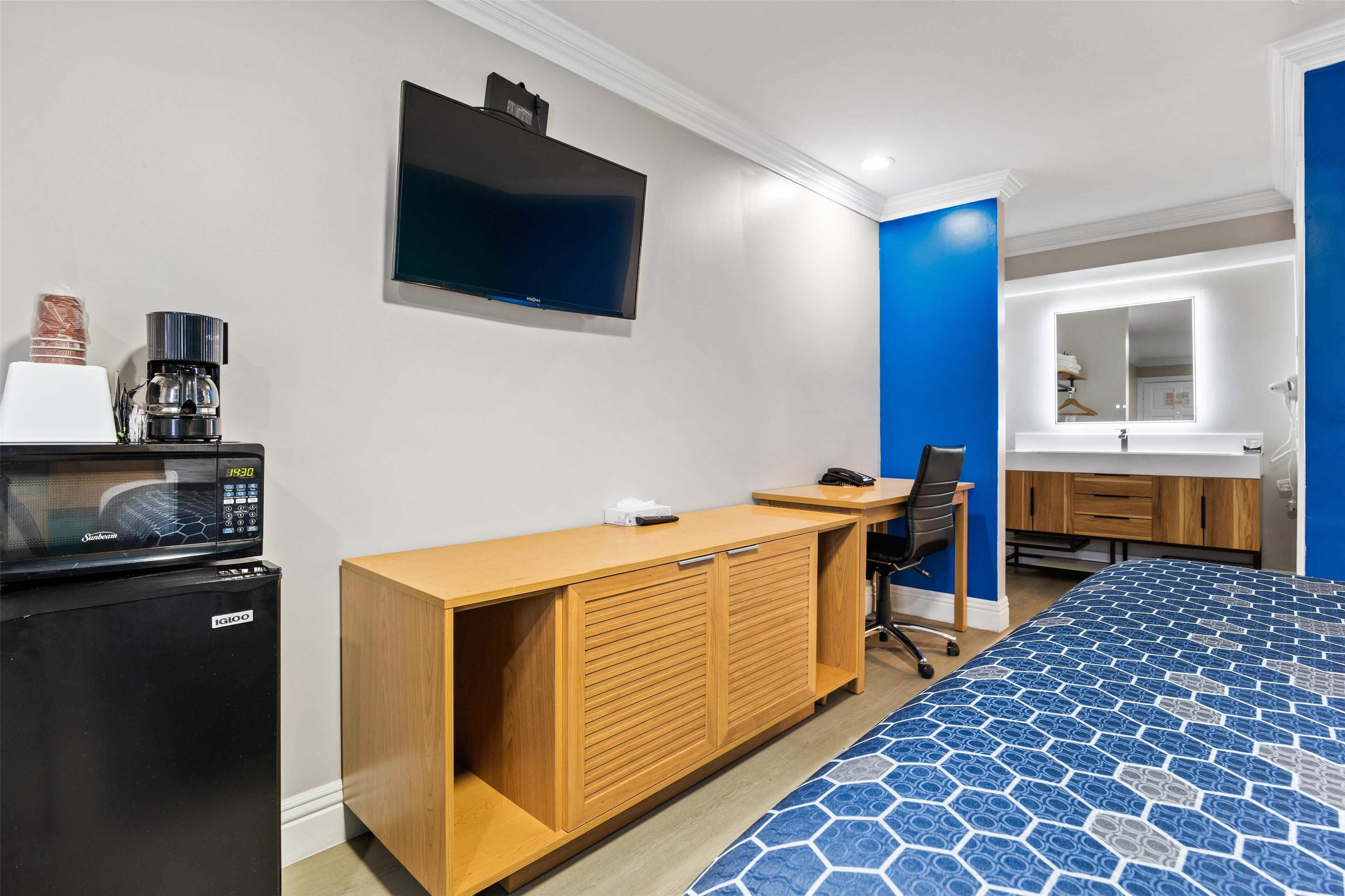 Habitación de hotel con cama, escritorio, silla, televisión, microondas y cafetera.