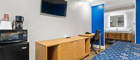 Une chambre d’hôtel équipée d’un lit, d’un bureau, d’une chaise, d’une télévision, d’un four à micro-ondes et d’une machine à café.