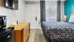 Hotellihuone, jossa on sänky, työpöytä, kahvinkeitin, seinälle asennettu televisio ja ovi, joka johtaa toiseen huoneeseen.
