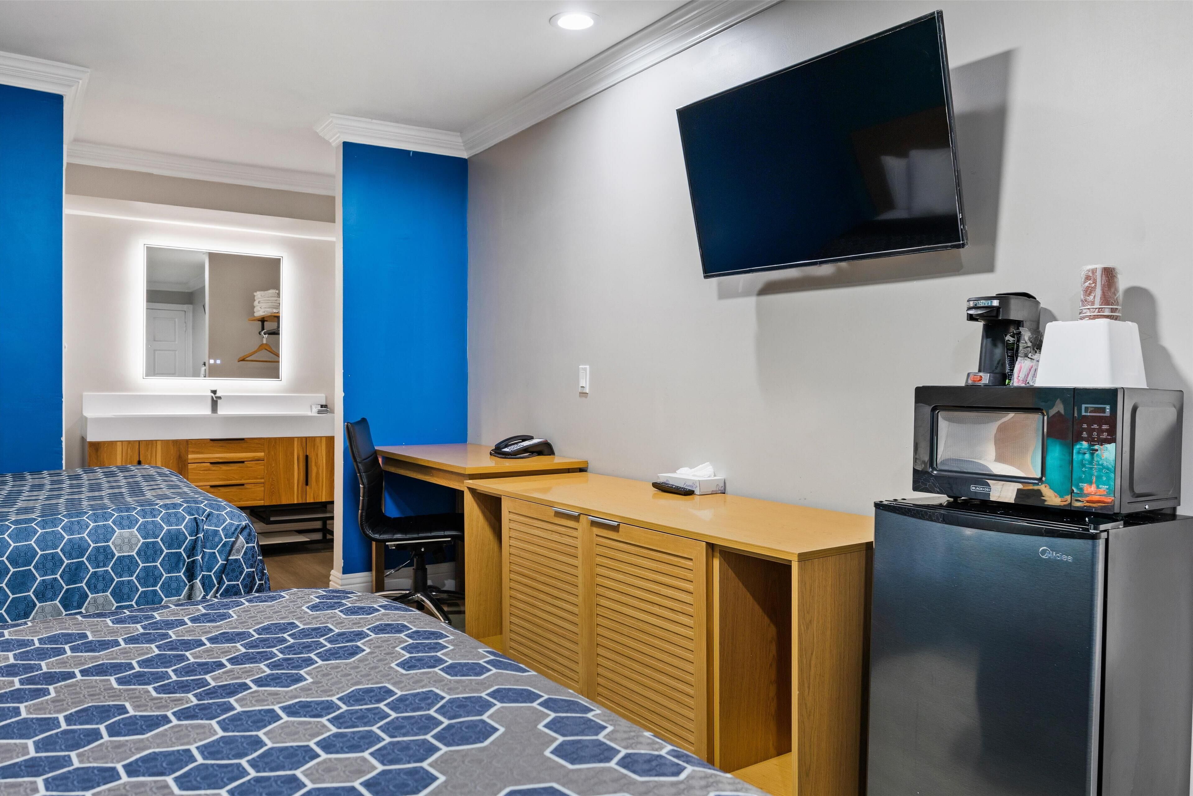 A hotel room with a bed, a desk, a refrigerator, a microwave, a TV, and a mirror.