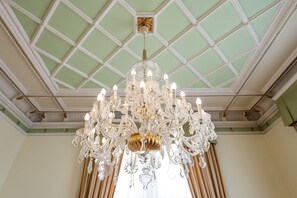 Een weelderige kroonluchter met meerdere lampen, hangend aan een hoog plafond, omgeven door decoratieve ornamenten en een groen geschilderd plafond.