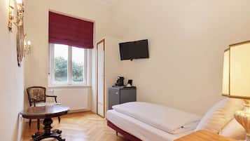 A bedroom with a bed, a desk, a chair, a television, and a radiator.