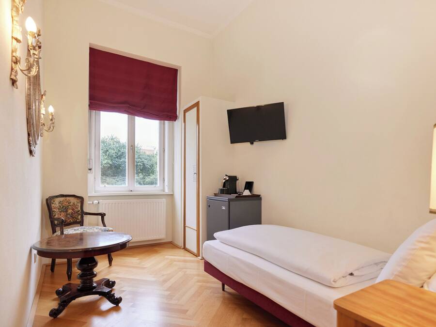 A bedroom with a bed, a desk, a chair, a television, and a radiator.
