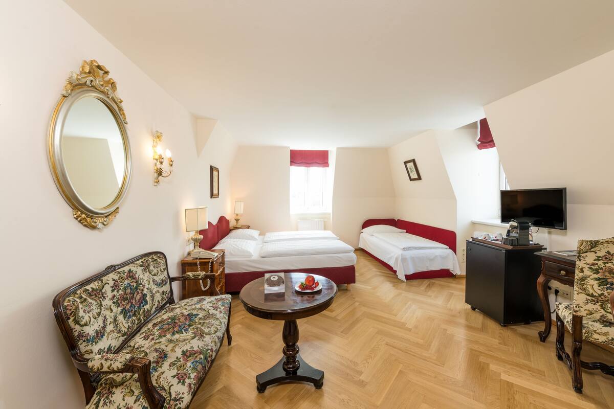 Een hotelkamer met een bed, twee nachtkastjes, een stoel, een kleintje tafeltje, een televisie en een spiegel.