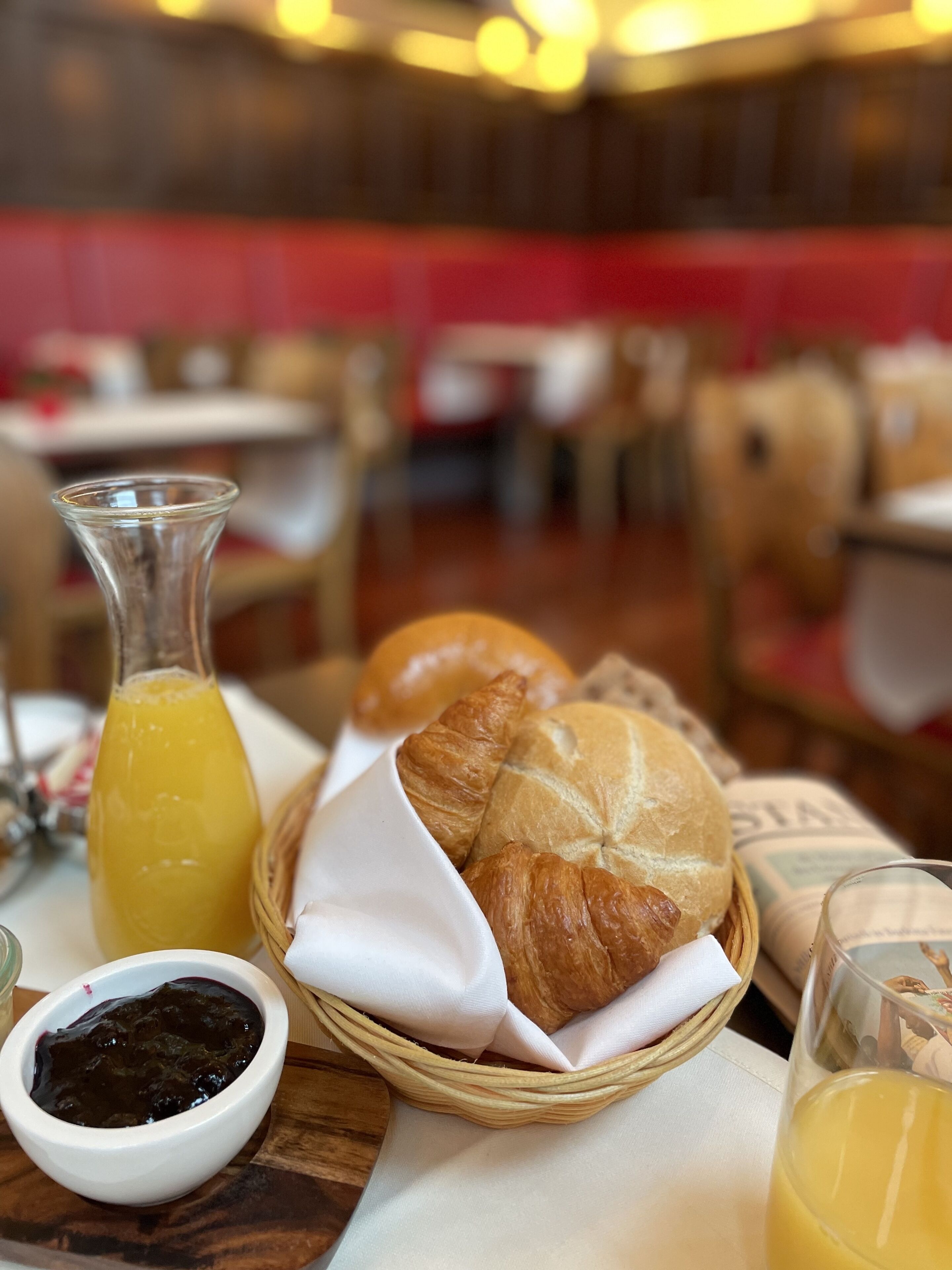 A dining table with a basket containing croissants, a bottle of orange juice, and a small bowl of jam.
