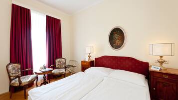 A hotel room with a large bed, two chairs, a small table, a nightstand with a lamp, and a painting on the wall.