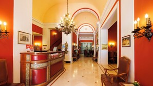 A hotel lobby with a reception desk, a staircase, and a chandelier. - Hotel Regina (Vienna)