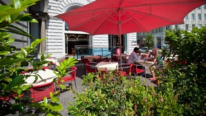 An outdoor cafe with red umbrellas, red wicker chairs, and tables. - Hotel Regina (Vienna)