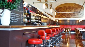 Un grand espace bar doté d’un long comptoir, de nombreux tabourets de bar rouges et d’une plante en pot.